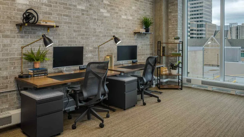 Semi-private office workstations along a windowed brick wall